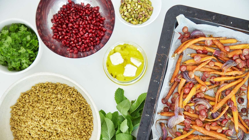 Salad ingredients including cooked freekeh, fresh parsley, mint, goat cheese, pomegranate seeds, pistachios, roasted vegetables.