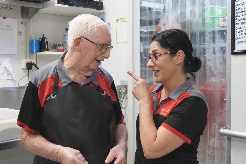 An old man and a woman talk in their butcher work clothes