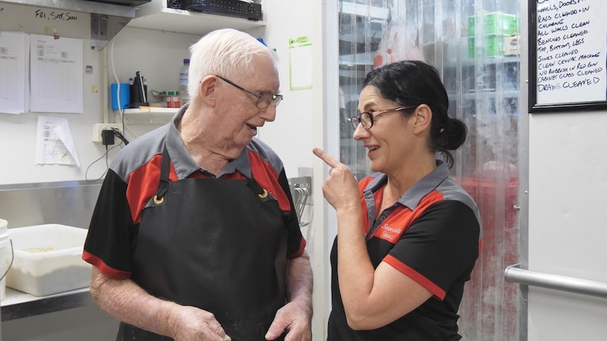 An old man and a woman talk in their butcher work clothes