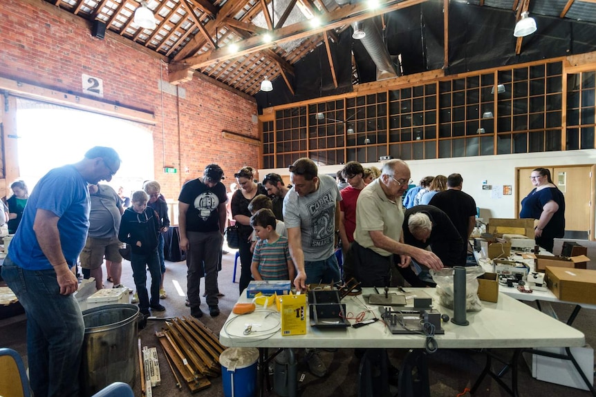 A crowd of people walking a u-shaped path in a large room, examining items on tables.