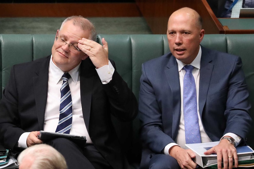 Morrison rubs his brow, sitting between Bishop and Dutton. Bishop has arms crossed. Dutton holding paperwork.