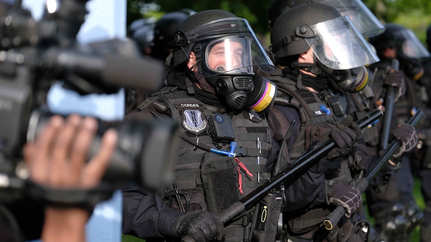 Man wearing police riot gear including black helmet, mask and shield