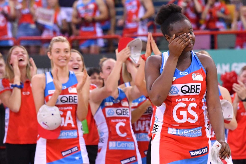 NSW Swifts player Sam Wallace wipes away a tear on the court. Her teammates cheer behind her.