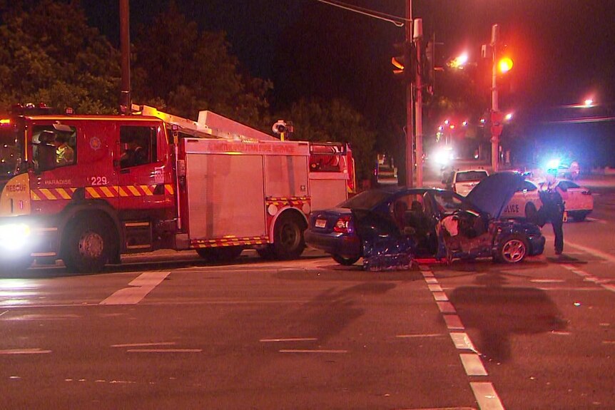 A fire truck and a blue sedan with considerable damage in an intersection at night