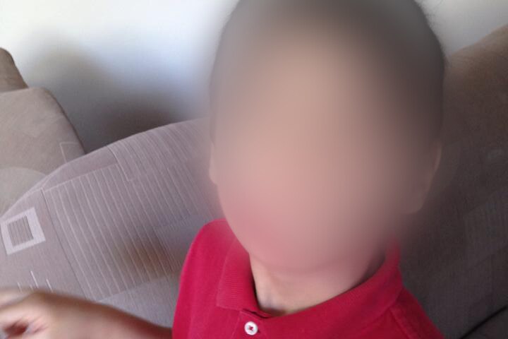 A boy dressed in red poses for a photo. His face is blurred.