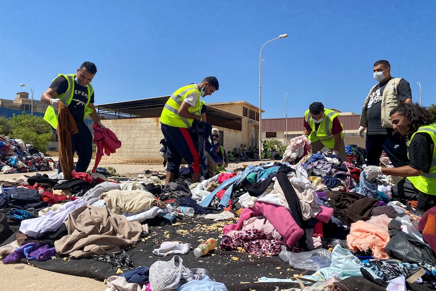 A group of volunteers wearing fluorescent vests sort through a pile of clothing laid out on a blanket outside