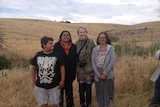 A group of people standing on a hill covered in dry grass overlooking a cleared area where an old homestead once stood.