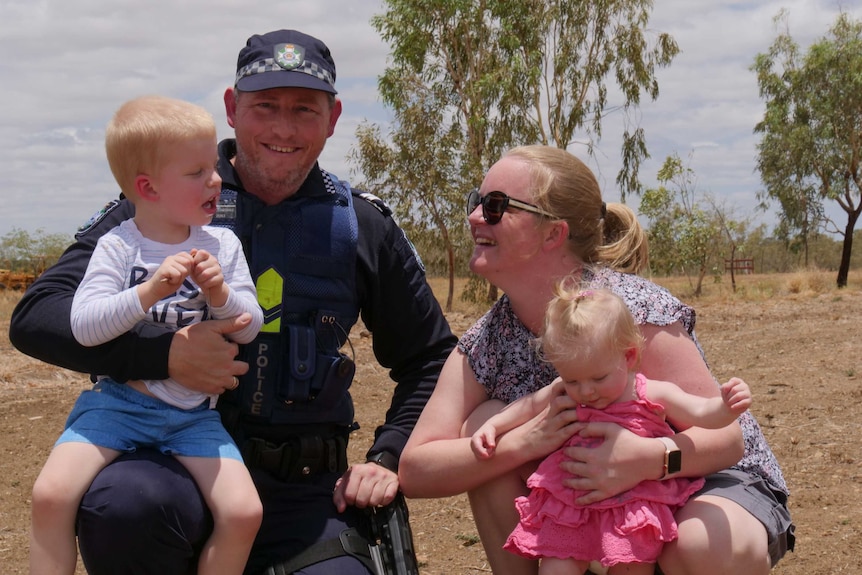 Kynuna police officer in charge Senior Constable Graeme Ferguson kneels in the red dirt with his wife and two young children.