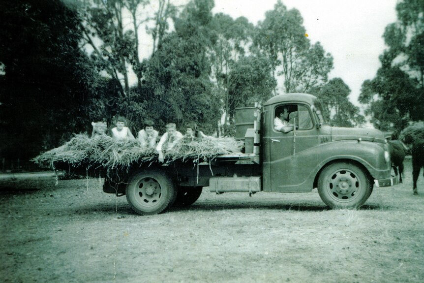 An old photo of a truck with some people on the back lying on hay.