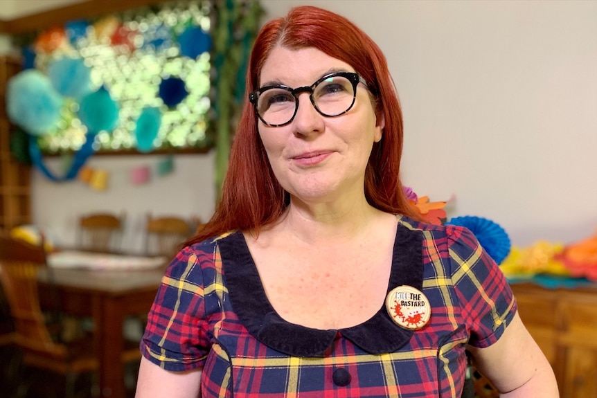 Sam Connor wearing glasses and a tartan dress, smiling at the camera.