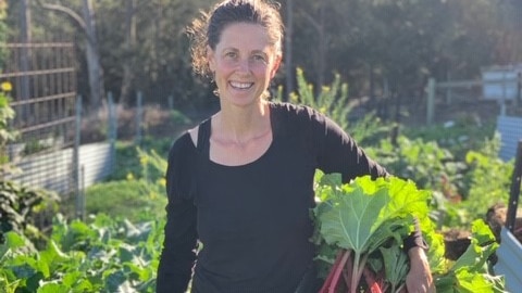 A woman stands in a garden with rhubarb under her arm.