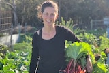 A woman stands in a garden with rhubarb under her arm.