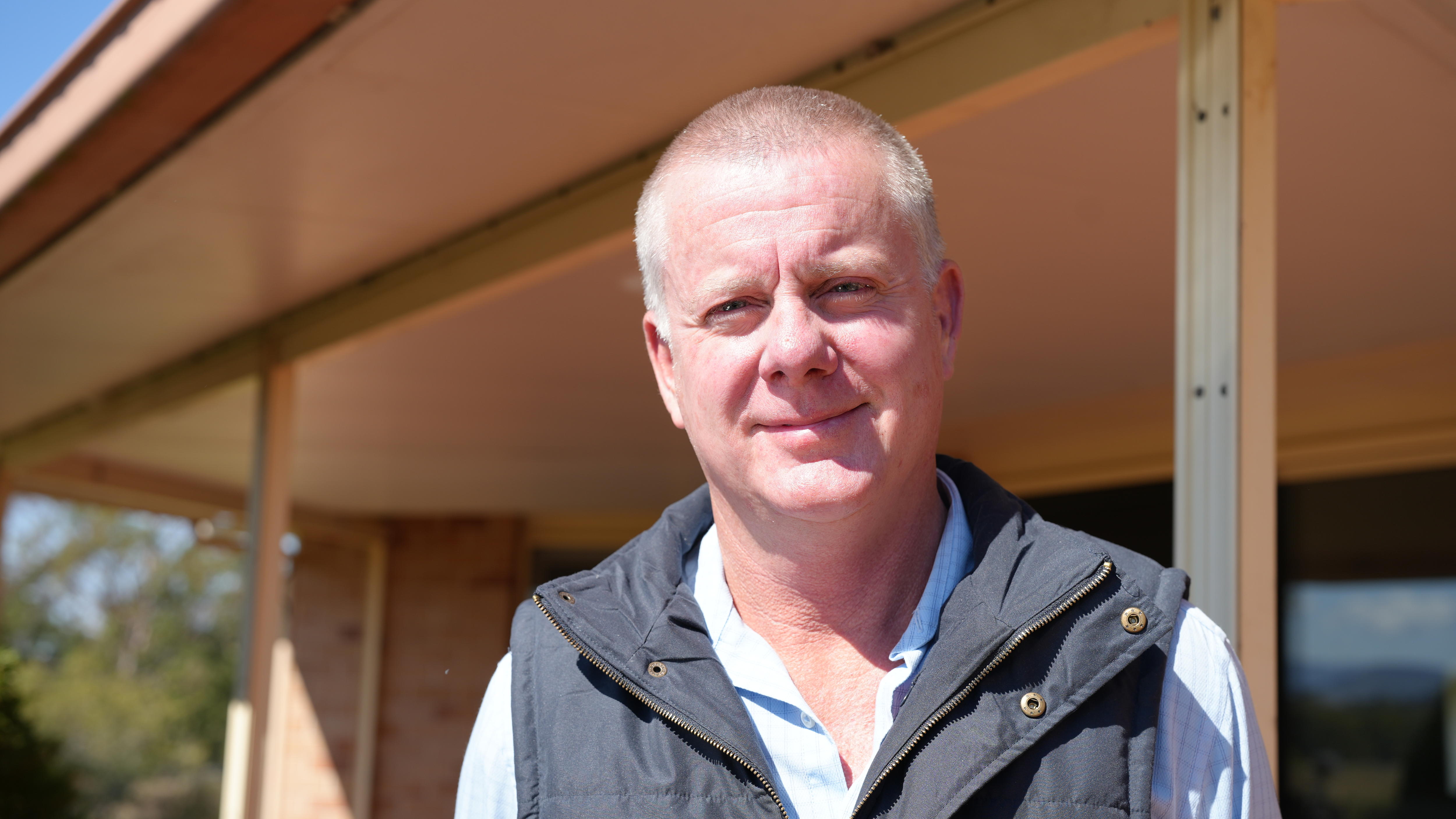 A smiling man with very short hair, wearing a dark down jacket over a light shirt.