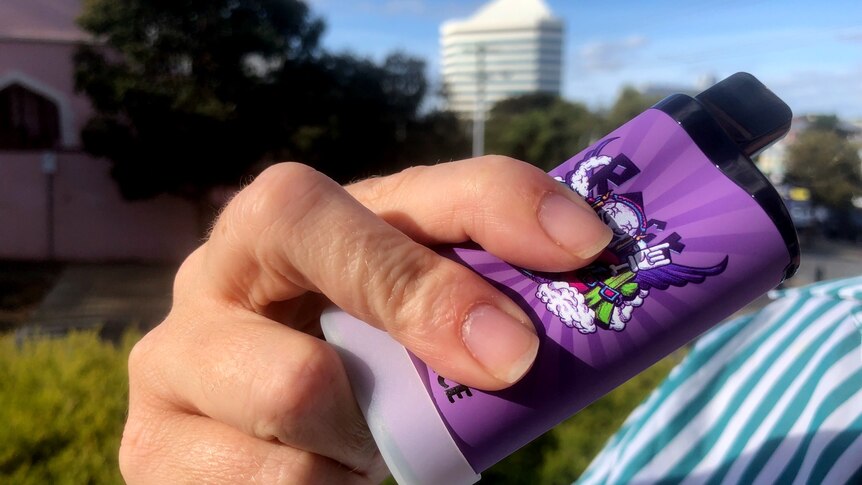 A hand holding a purple vape, Bunbury tower in the background