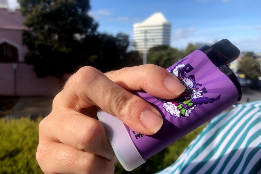 A hand holding a purple vape, Bunbury tower in the background