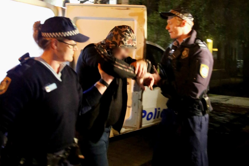 a man being pulled out of a police van by two officers