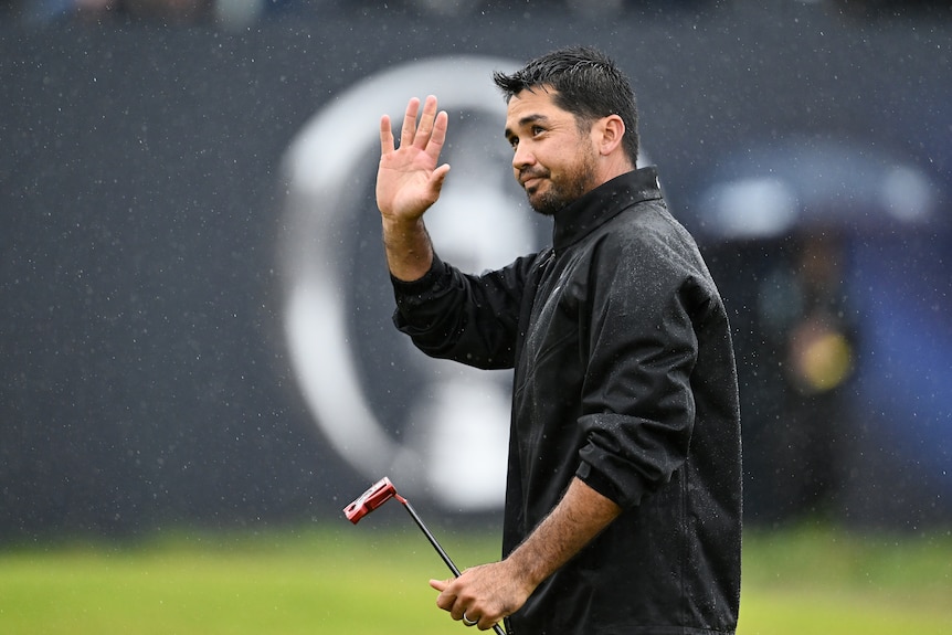 A man waves to the crowd from the golf green in pouring rain.