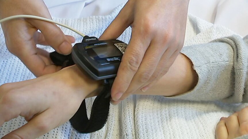 Nurse's hands fit a watch-style sensor on the wrist of cancer patient Aliona Grytsenko.