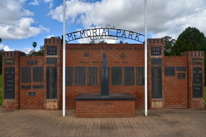 A brick wall with a 'Memorial Park' sign and bronze plaques.