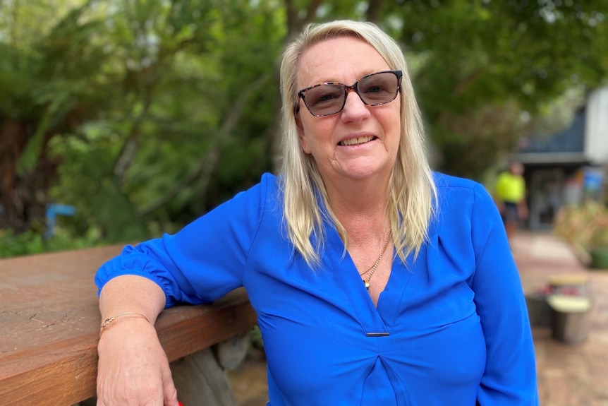 a woman smiles at the camera wearing a blue shirt and blonde hair