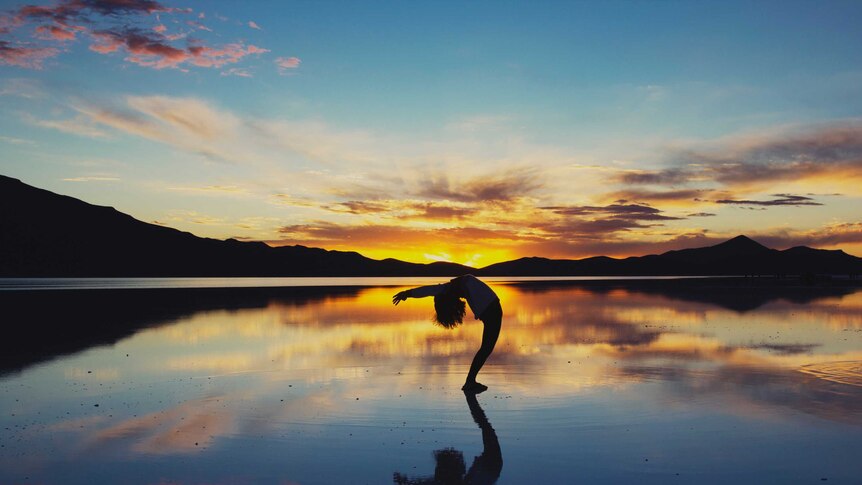 Person doing a backbend on a beach with the sun rising in the background.