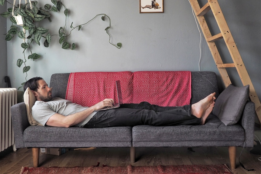 Alex McClintock stretched out across a sofa, using his laptop