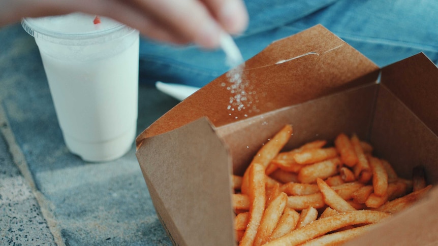 A box of chips with someone sprinkling salt on them