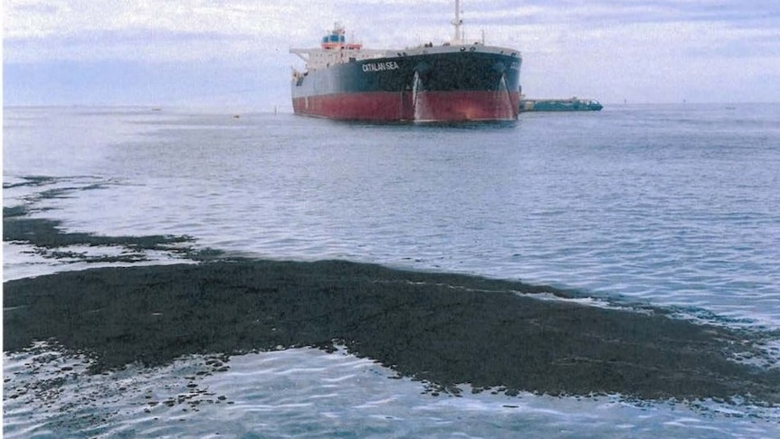 An oil slick on the ocean surface with a tanker in the background.