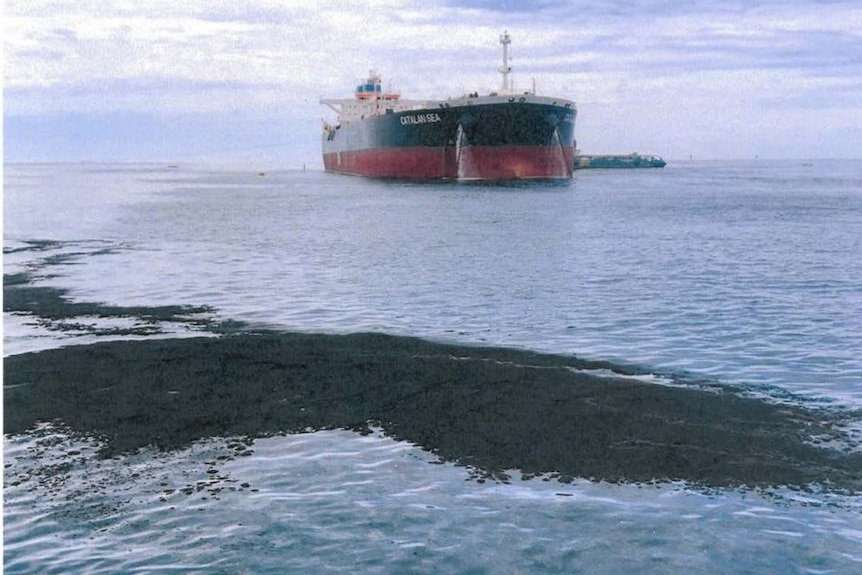 An oil slick on the ocean surface with a tanker in the background.