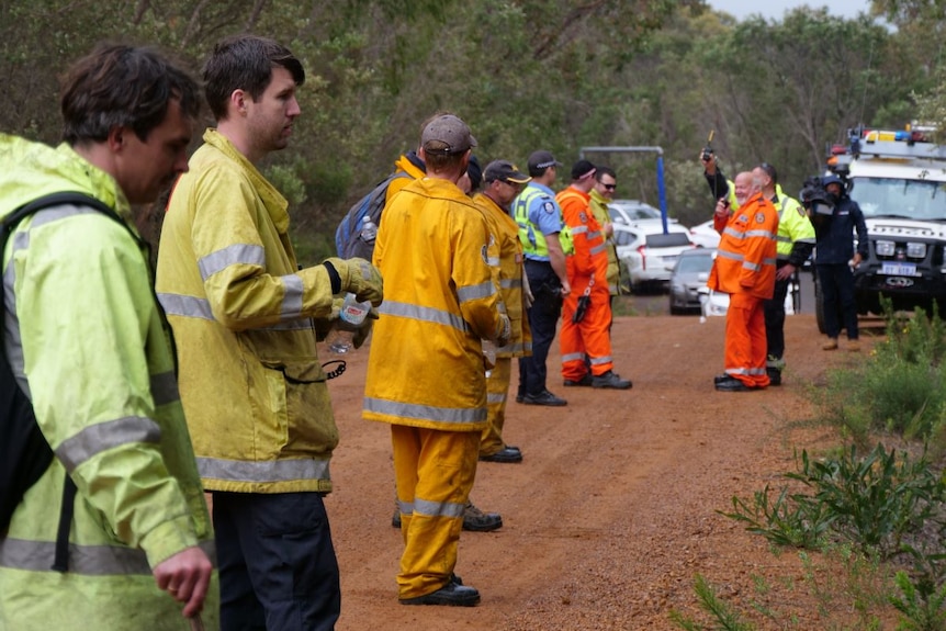 A row of men wearing high-vis clothing stand in a row next to bushland.