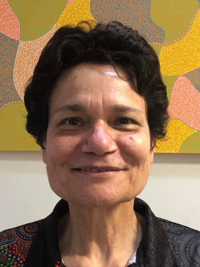 Mid shot of Corina Martin, who is smiling in front of a colourful Aboriginal art piece