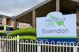 An ambulance is parked next to a brick building with a sign that reads Menarock Life Essendon out the front.