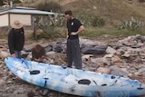 Three people next to a sea kayak on a rocky shore