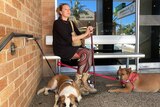 Woman with a walking stick wearing a black top sits with two dogs.