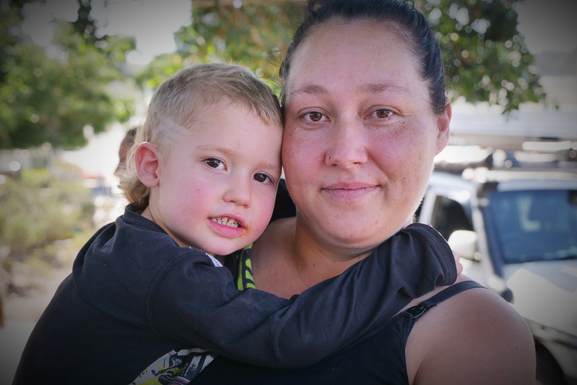 A close-up photo of a women holding her toddler, while the toddler smiles