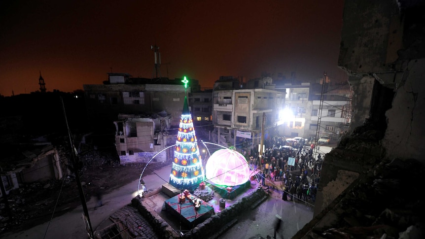 People gather by a Christmas tree near damaged buildings during Christmas eve in al-Hamidiyah neighbourhodd in the old city of Homs, Syria.