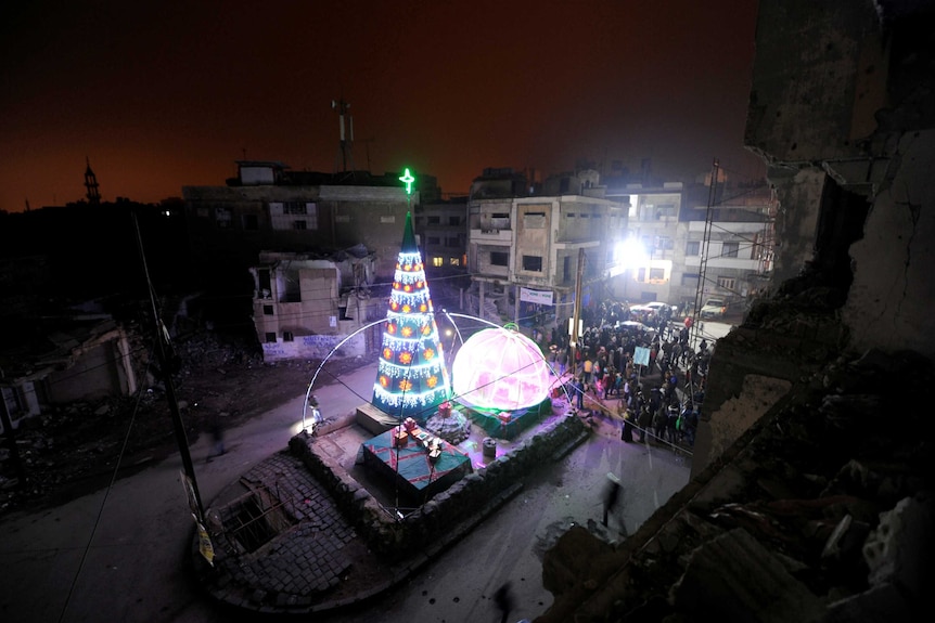 People gather by a Christmas tree near damaged buildings during Christmas eve in al-Hamidiyah neighbourhodd in the old city of Homs, Syria.