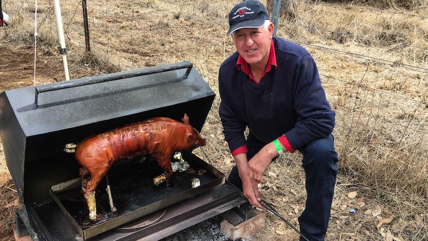 Farmer Geoff Bush squats beside the camp cooker he designed and built himself, in his shed.