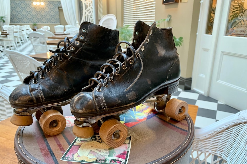 a pair of very old roller skates. they have wooden wheels and are made from black leather. they are sitting on an old case