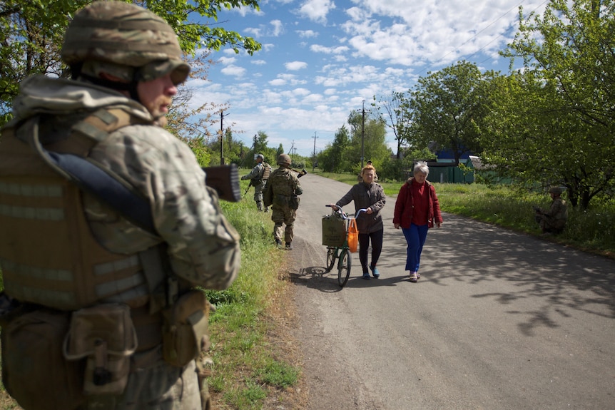 A group of women walking along a street as Ukrainian servicemen patrol.