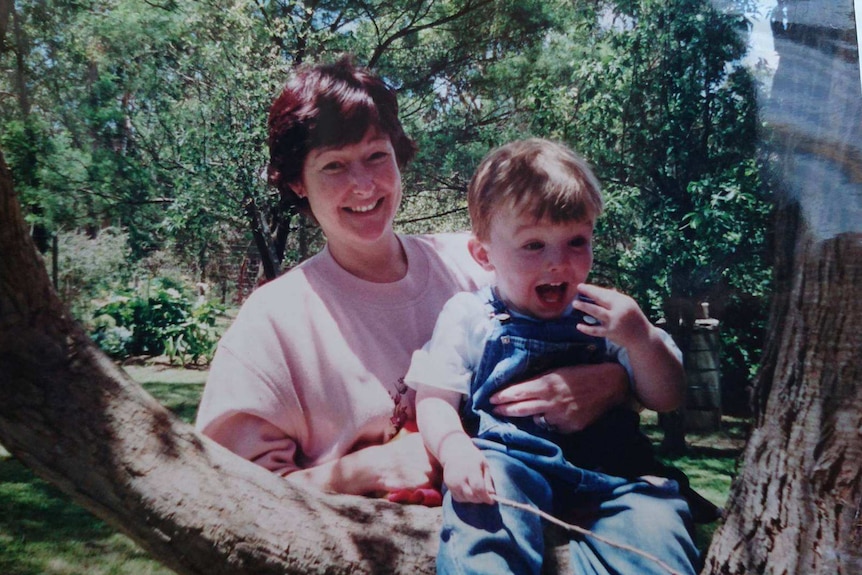 Myra holds her son sitting on a tree trunk when he was a baby