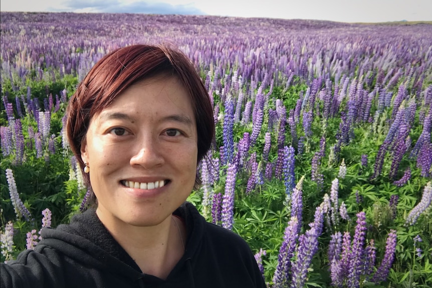 Een foto van een vrouw met kort haar die lacht in een veld met paarse bloemen.