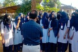 A group of school girls in hijabs talk to a man.