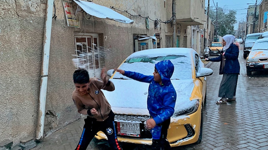 A child throws a snowball at another kid in the streets of Baghdad.