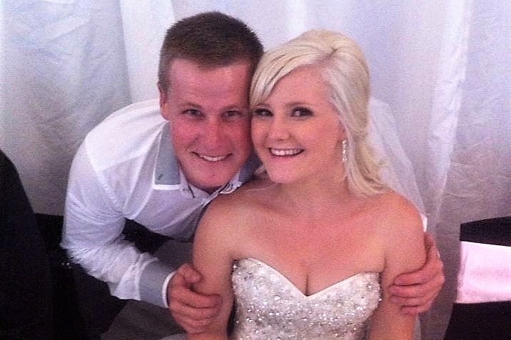 Bill Spencer sits behind his sister who is in wedding dress, with his arms around her.