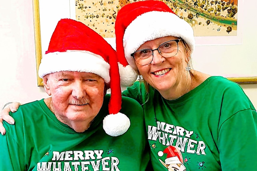 A man and woman smiling and wearing a red and white Santa hat and green Christmas shirt