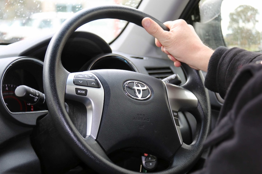 A hand on a car steering wheel.
