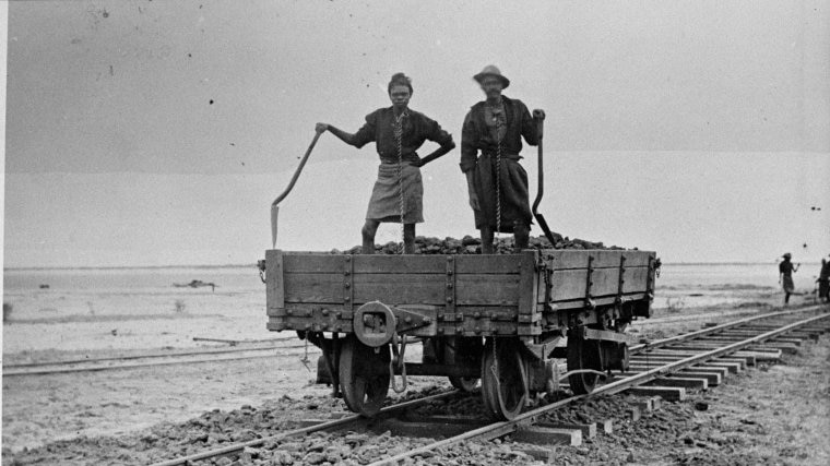 Indigenous people in chains working on jetty railway ballast laying.
