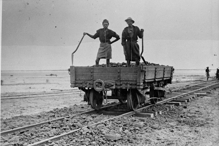 Indigenous people in chains working on jetty railway ballast laying.