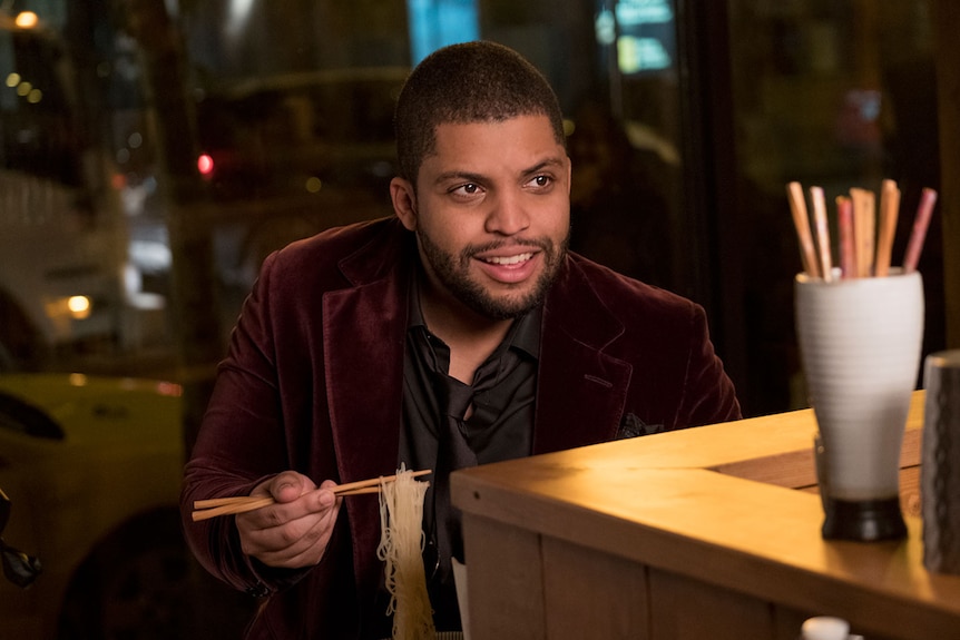 Colour close-up still of O'Shea Jackson Jr. seated at a restaurant and holding up chopsticks and noodles in 2019 film Long Shot.